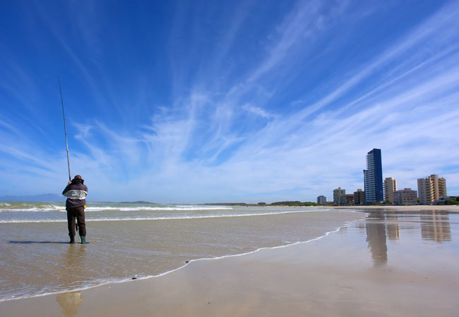 An angler fishing from a wide sandy beach with apartment blocks along the shoreline