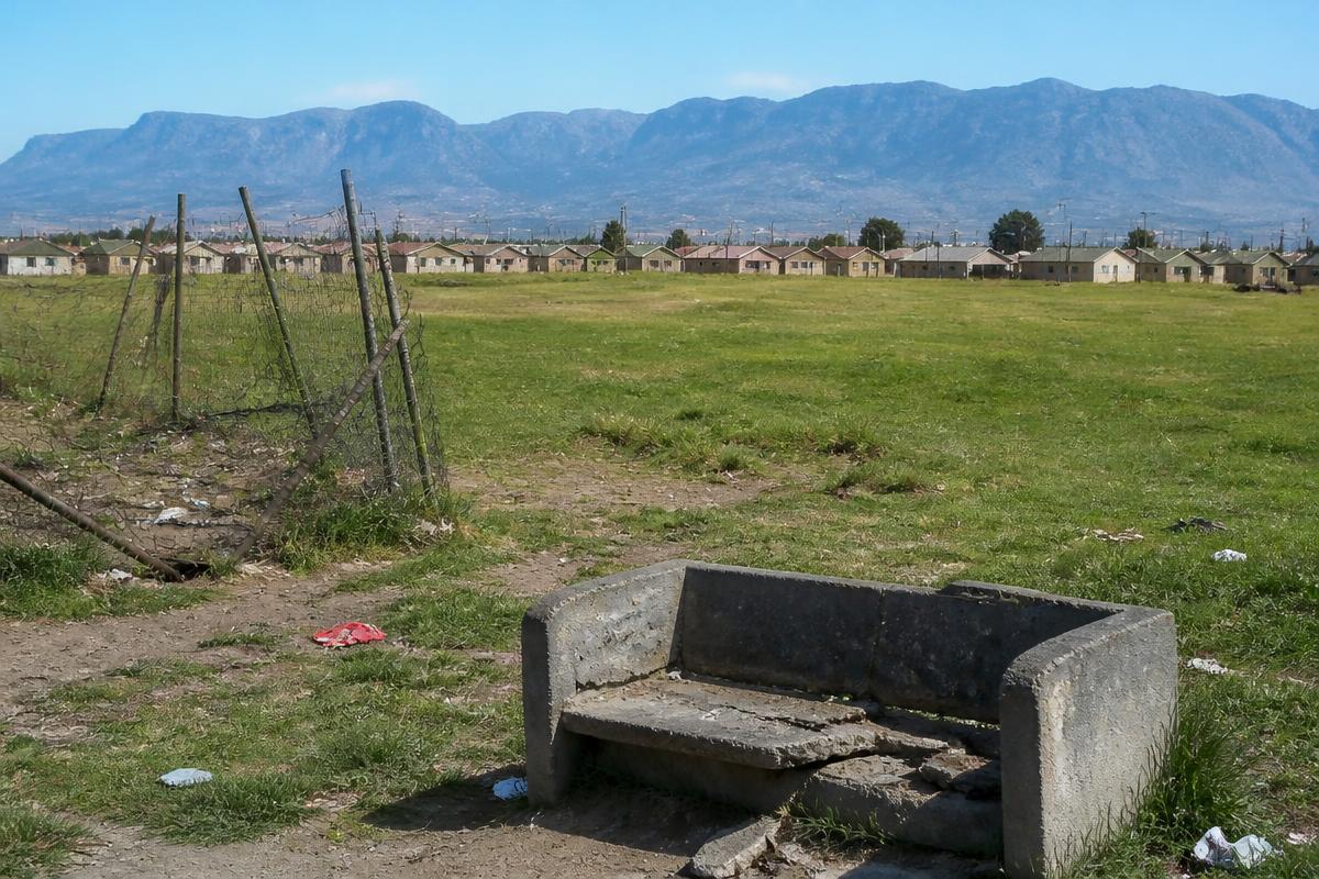 A neglected open municipal field with litter and a broken bench below the mountains